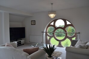 A modern living room with a large window, a flat-screen TV, and a chandelier.