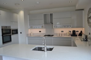 A modern kitchen with built-in appliances, a central island with a sink, and a clock on the wall.