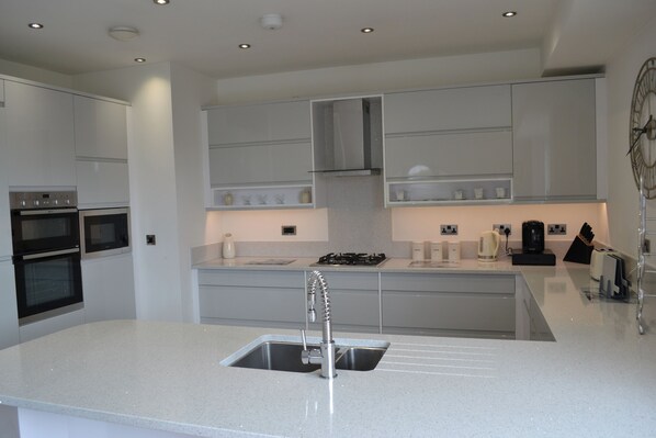 A modern kitchen with built-in appliances, a central island with a sink, and a clock on the wall.