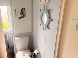 A bathroom with a toilet, a seahorse decoration, a ship's wheel mirror, and a towel rack.