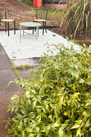 An outdoor seating area with a table and chairs, surrounded by greenery and a patterned mat.