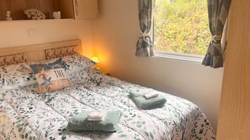 A bedroom with a bed, a nightstand, a window with curtains, and a shelf with decorative items.