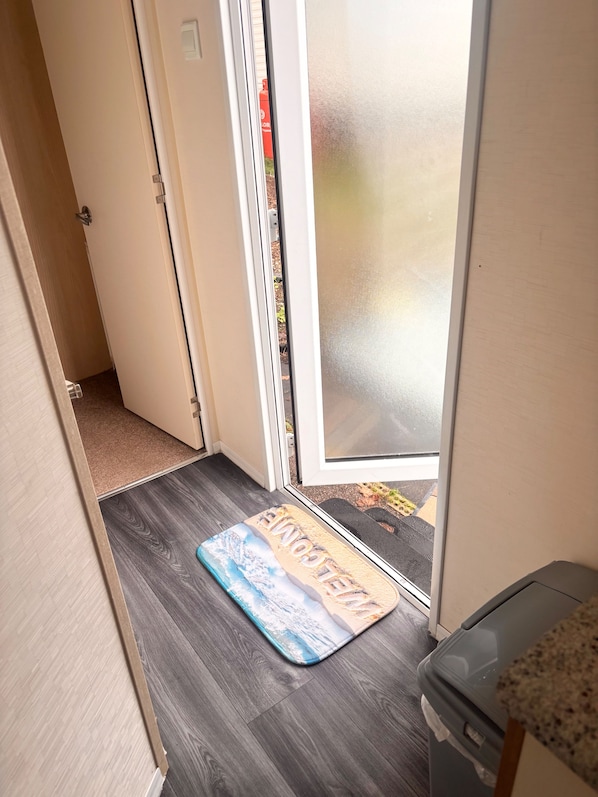A hallway with a doormat, a door, and a trash bin.