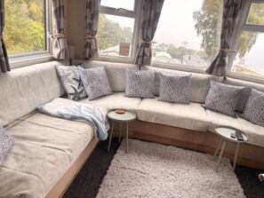A modern living room with a sectional sofa, patterned cushions, a small round table, and a view of the outdoors through large windows.