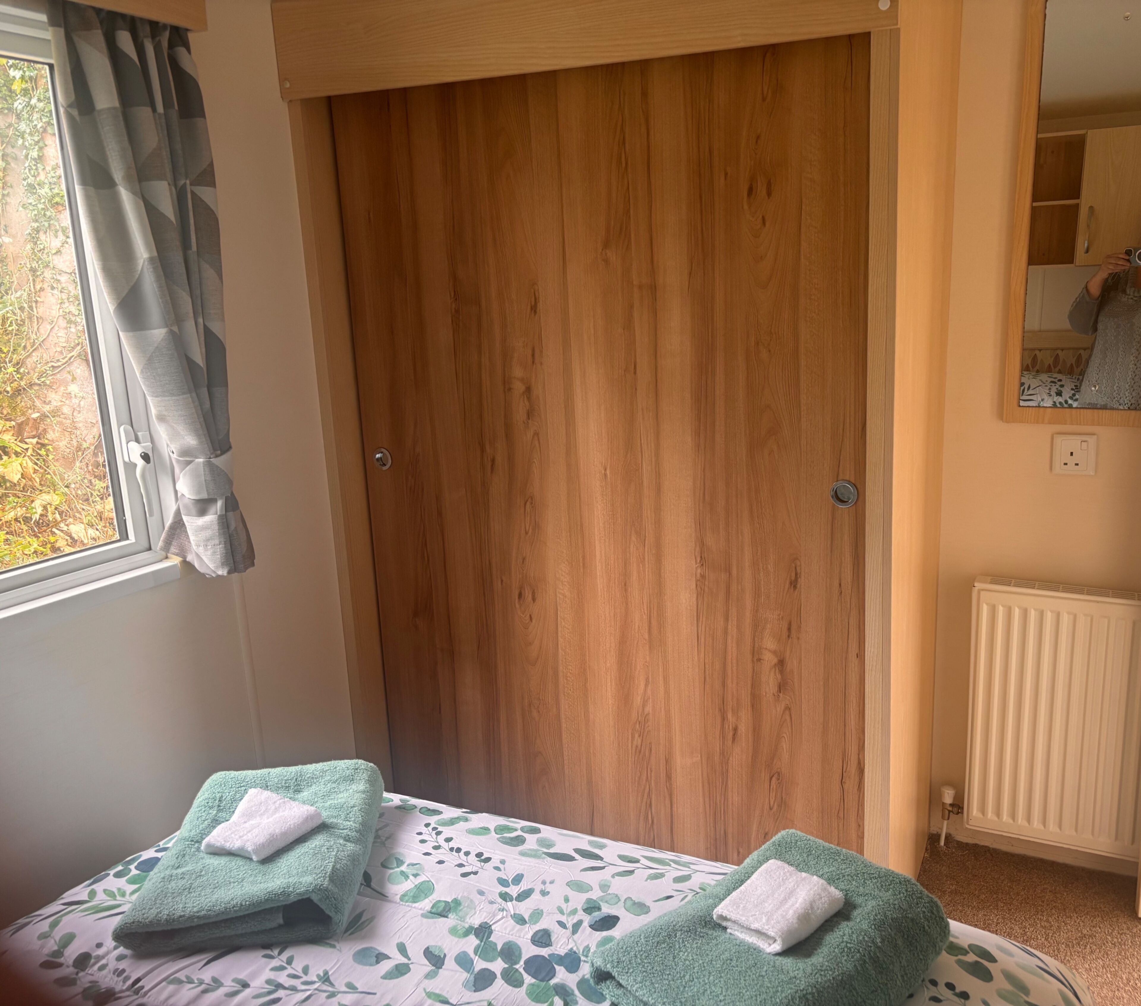 Une chambre avec une armoire en bois, un lit recouvert d’une couvre-lit à motifs floraux et une fenêtre avec des rideaux.