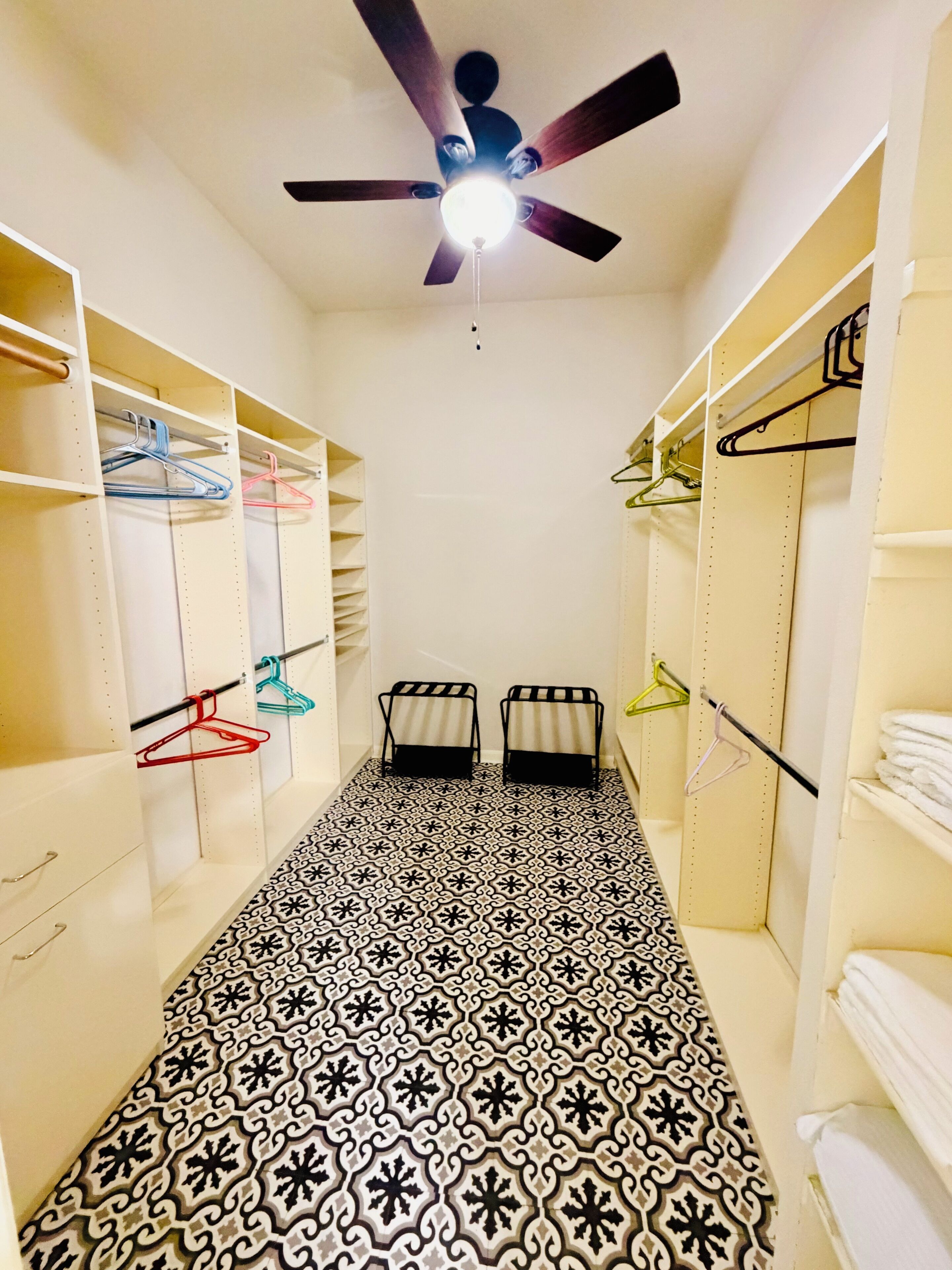 Un couloir étroit doté d’un sol à motifs, d’un ventilateur de plafond et d’étagères avec des porte-manteaux.