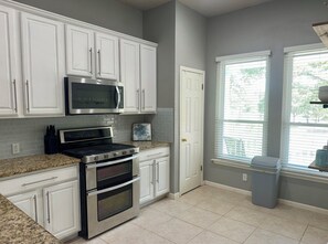 A kitchen with white cabinets, a microwave, a stove, and a window with blinds. - The Witte Estate - 5BR Main House + Apartment (Kyle)