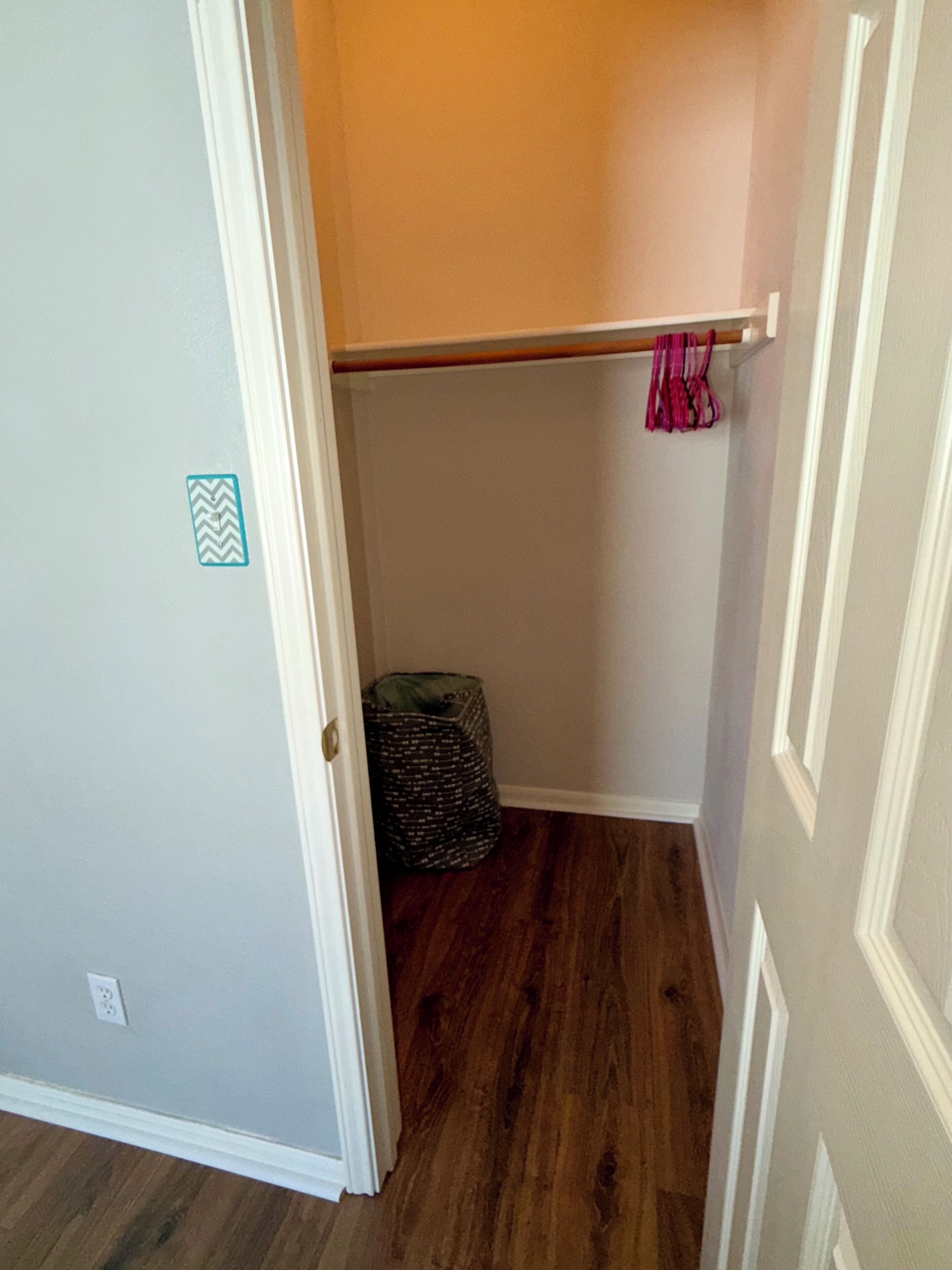 Un placard avec un plancher en bois, une tringle et un sac.