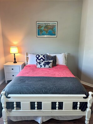 A bed with a white frame, a red and gray bedspread, and a world map above it. - The Witte Estate - 5BR Main House + Apartment (Kyle)
