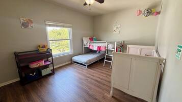 Une chambre d’enfant avec un lit superposé, un bureau, un ventilateur de plafond et une fenêtre.