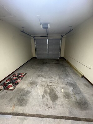Eine Garage mit geschlossenem Garagentor, Betonboden und einem Teppich mit Blumenmuster.