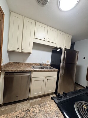 Una cocina con armarios blancos, un refrigerador de acero inoxidable y un lavavajillas.