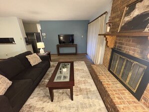 A living room with a sofa, coffee table, TV, fireplace, and a patterned rug.