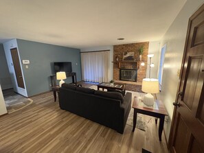 A living room with a sofa, a television, a fireplace, and a door.