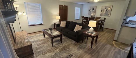 A living room with a sofa, coffee table, and lamps. There is a dining area with a table and chairs.