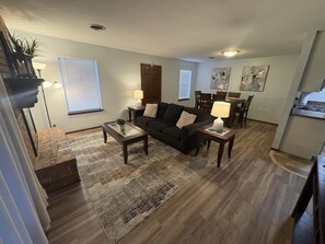 Una sala de estar con sofá, mesa de centro y lámparas. Hay una zona de comedor con mesa y sillas.