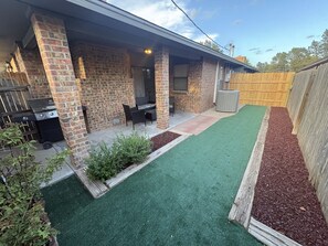 Ein Garten mit Pflasterterrasse, Gartenmöbeln, einem Grill und künstlichem Rasen.