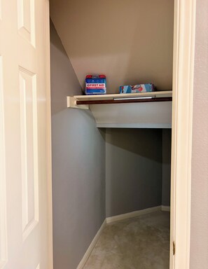 A corner of a room with a door, a shelf with first aid kit and a box of tissues, and a carpeted floor. - Witte Manor - Spacious 4BR Retreat (Kyle)