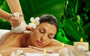 A person receiving a massage with a flower in their hair, surrounded by white flowers and candles. - Courtyard Siliguri (Siliguri)