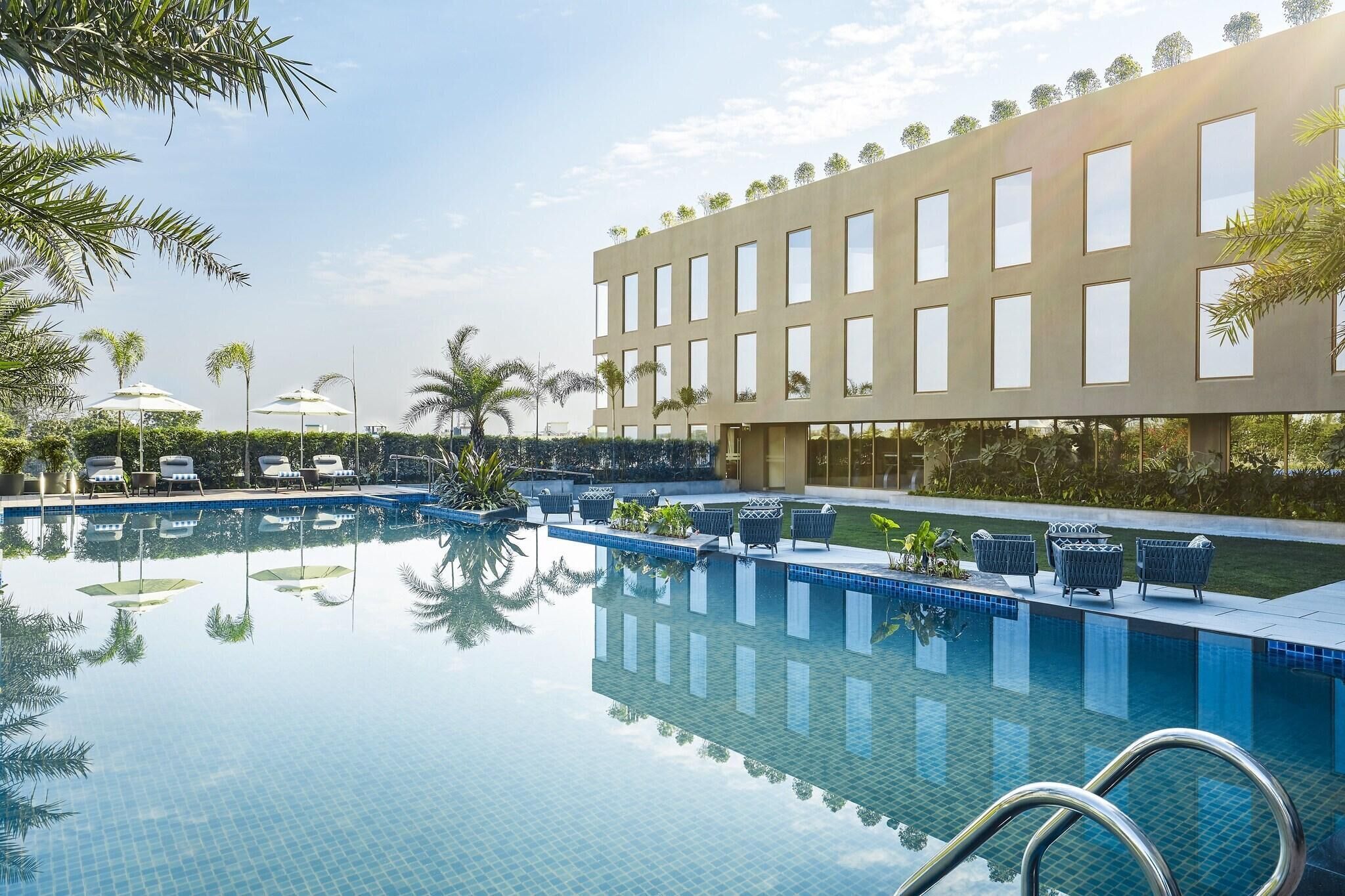 A swimming pool with lounge chairs and umbrellas, surrounded by a building with large windows.