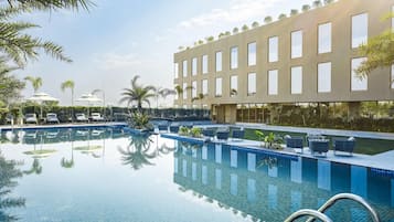A swimming pool with lounge chairs and umbrellas, surrounded by a building with large windows.