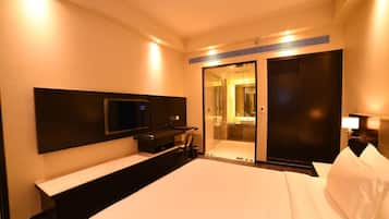 A hotel room with a bed, a TV mounted on the wall, a desk with a chair, a mirror, and a sliding door leading to a bathroom.