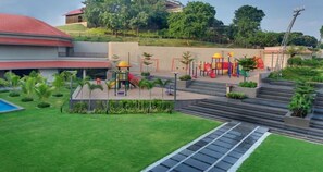 A playground with slides and swings, surrounded by a landscaped area with grass and small plants.