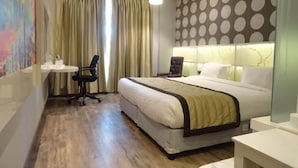 A hotel room with a bed, a desk, a chair, and a large window with curtains. - Hotel Orange (Agra)