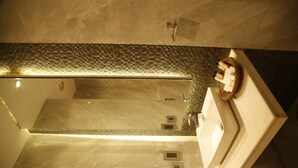 A modern bathroom with a glass shower enclosure, a white sink, and a tiled backsplash. - Hotel Orange (Agra)