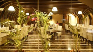 A restaurant with a modern interior, featuring a central staircase, white dining tables, and potted plants. - Hotel Orange (Agra)