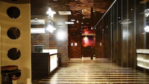 A modern hotel lobby with a long reception desk, a staircase, and a wall with circular mirrors. - Hotel Orange (Agra)