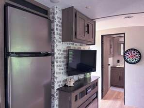 Una cocina moderna con refrigerador integrado, televisor de pantalla plana, armarios de madera y un dardo en la pared.