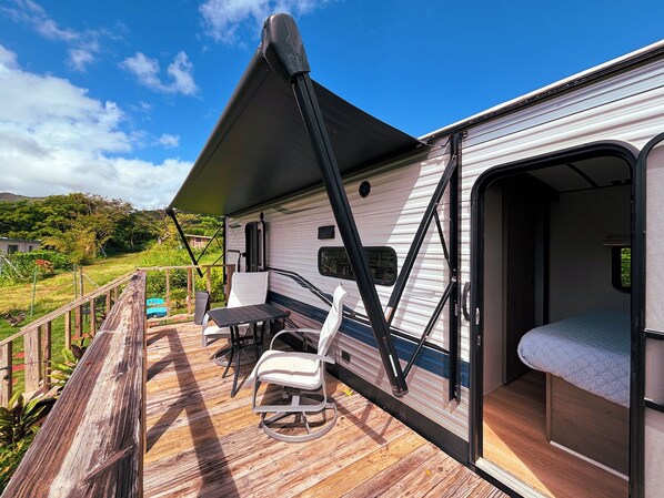 Una casa móvil con un porche, una zona de comedor con sillas y una mesa, y un dormitorio con cama.