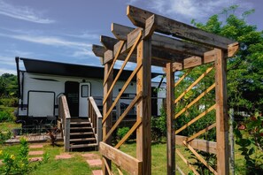 A wooden pergola structure with a staircase leading to a white RV parked in a garden.