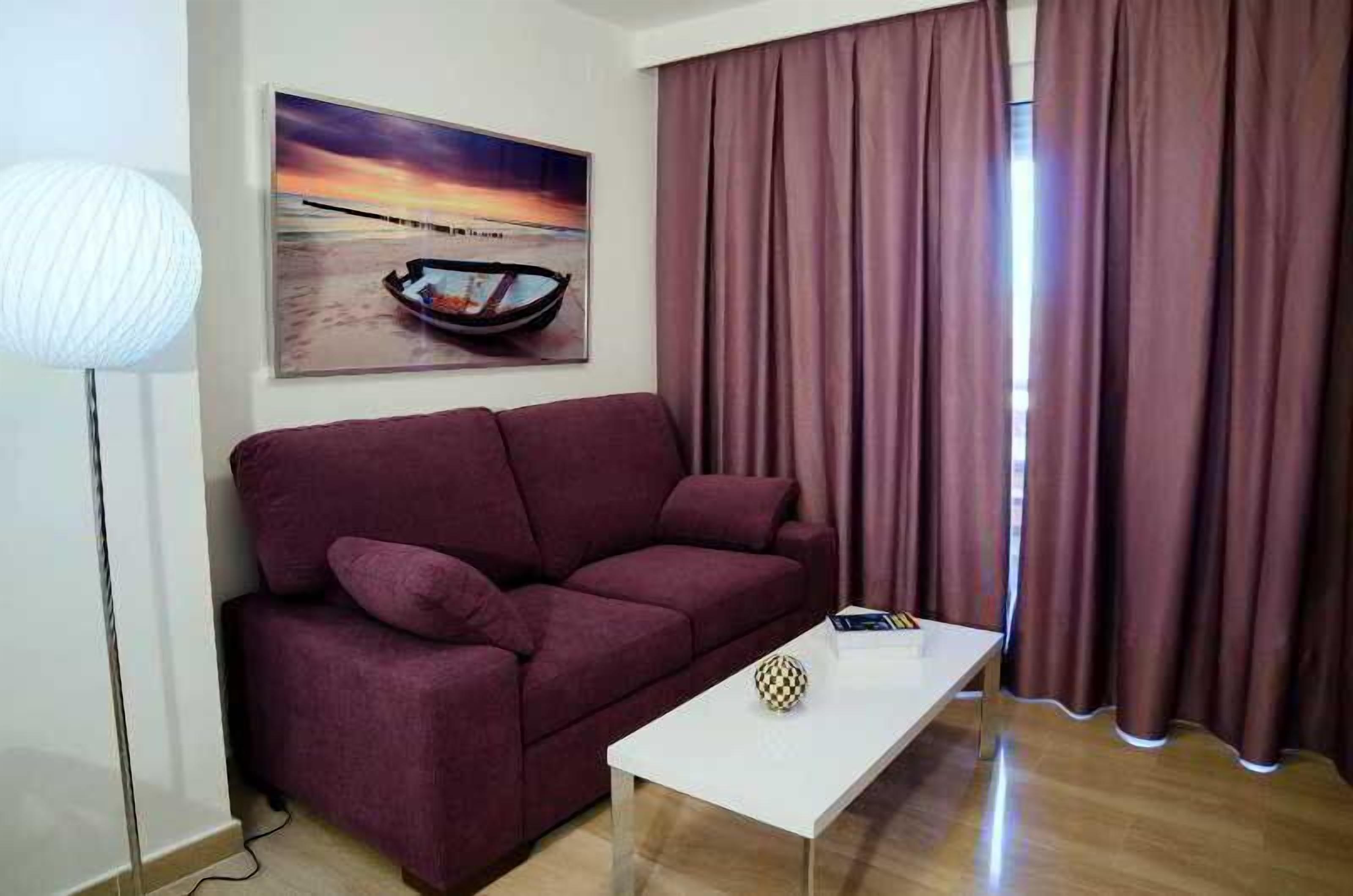 Una sala de estar con un sofá, una mesa de centro, una lámpara y un cuadro de un barco en la playa.