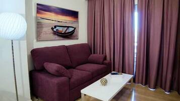 Una sala de estar con un sofá, una mesa de centro, una lámpara y un cuadro de un barco en la playa.