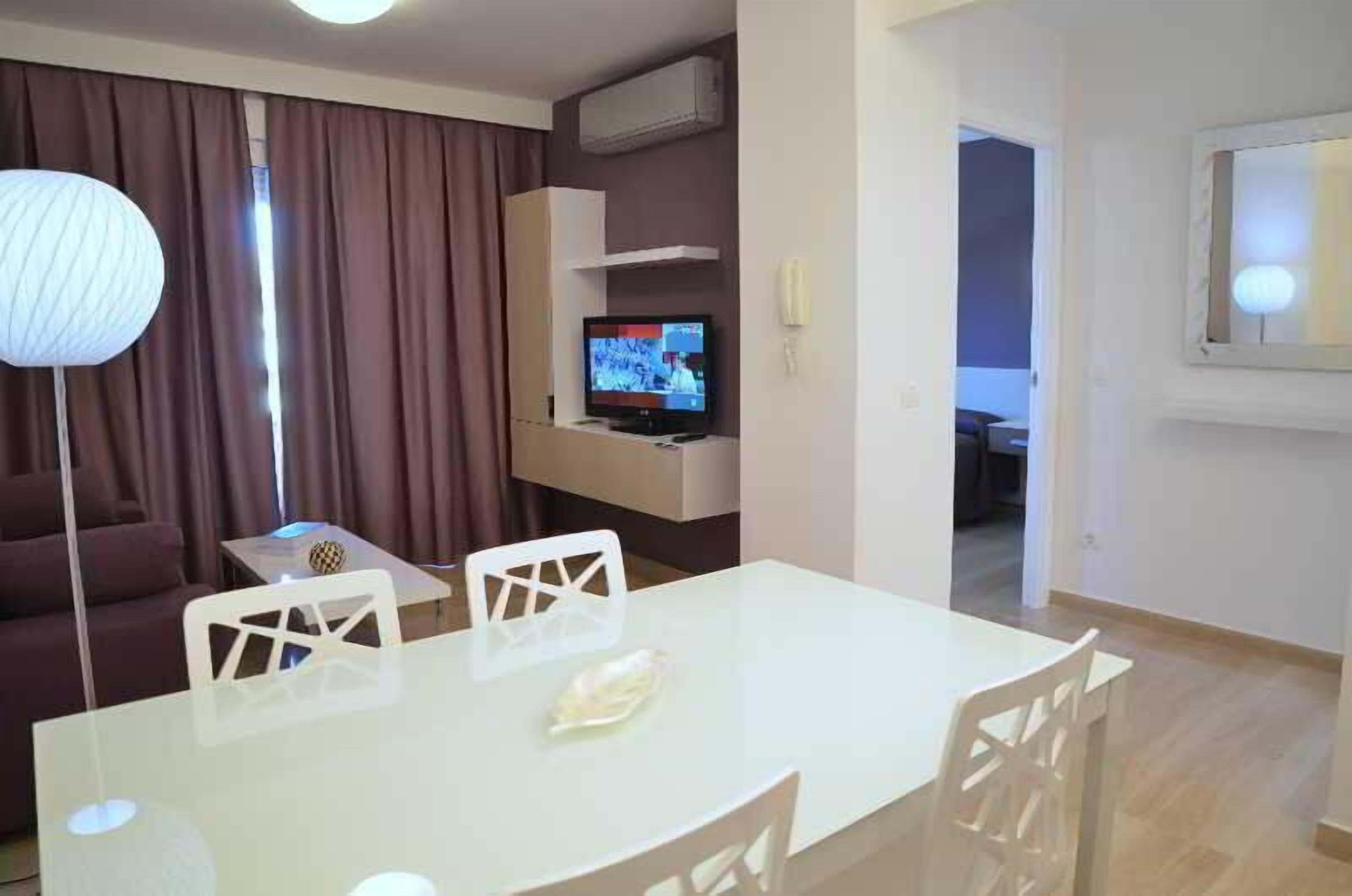 Una sala de estar moderna con comedor, televisor de pantalla plana y un gran ventanal con cortinas.