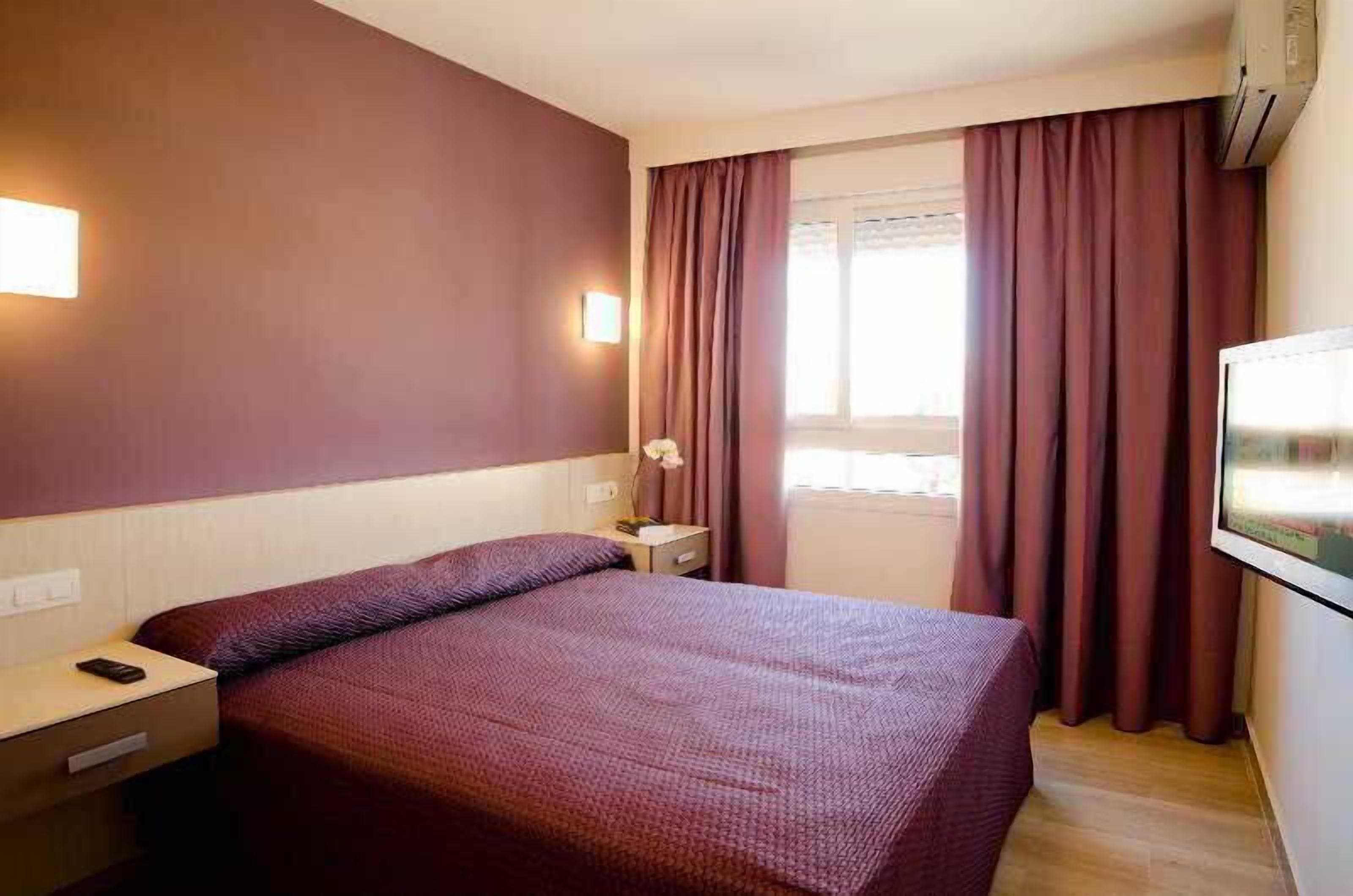 A hotel room with a bed, nightstand, bedside lamp, and a television.