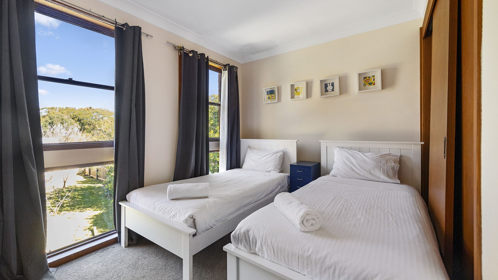 Ein Hotelzimmer mit zwei Betten, einem Fenster mit Vorhängen, einem Nachttisch und einer Wand mit gerahmten Bildern.