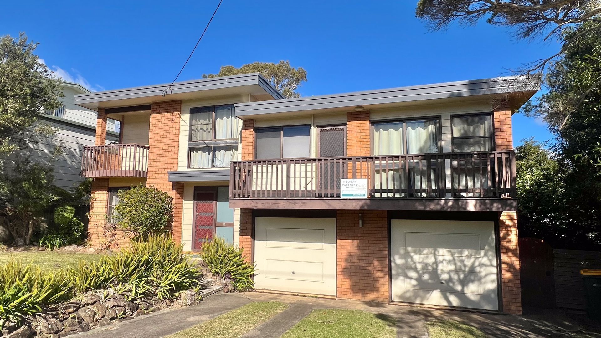 A two-story residential building with a balcony on the upper floor, a garage, and a well-maintained front yard.