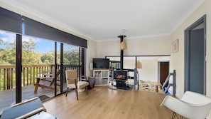 A spacious living area with a fireplace, wooden flooring, and a balcony with a view of trees. - Aqua, Pet Friendly Holiday Home Close to the Beach (Manyana)
