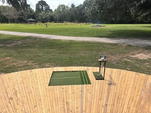 A wooden deck with a green artificial turf area, a metal basket, and a small table.