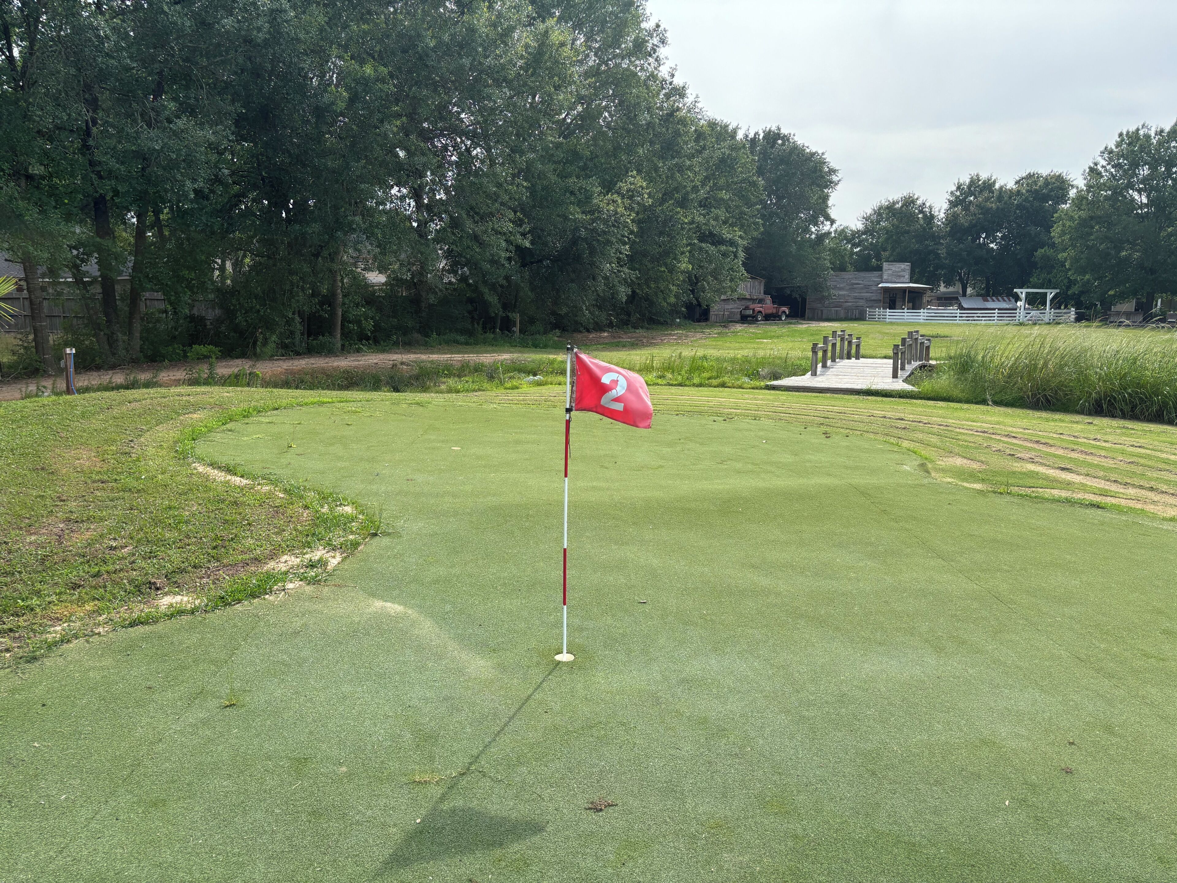 Een golfbaan met een vlaggenstok met het nummer 2, omringd door goed onderhouden gras en bomen.