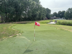 En golfbana med en flaggstång som är märkt med siffran 2, omgiven av välskött gräs och träd.