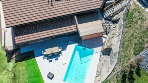Et luftfoto af et hus med swimmingpool, terrasse med udendørs møbler og en lille træterrasse.