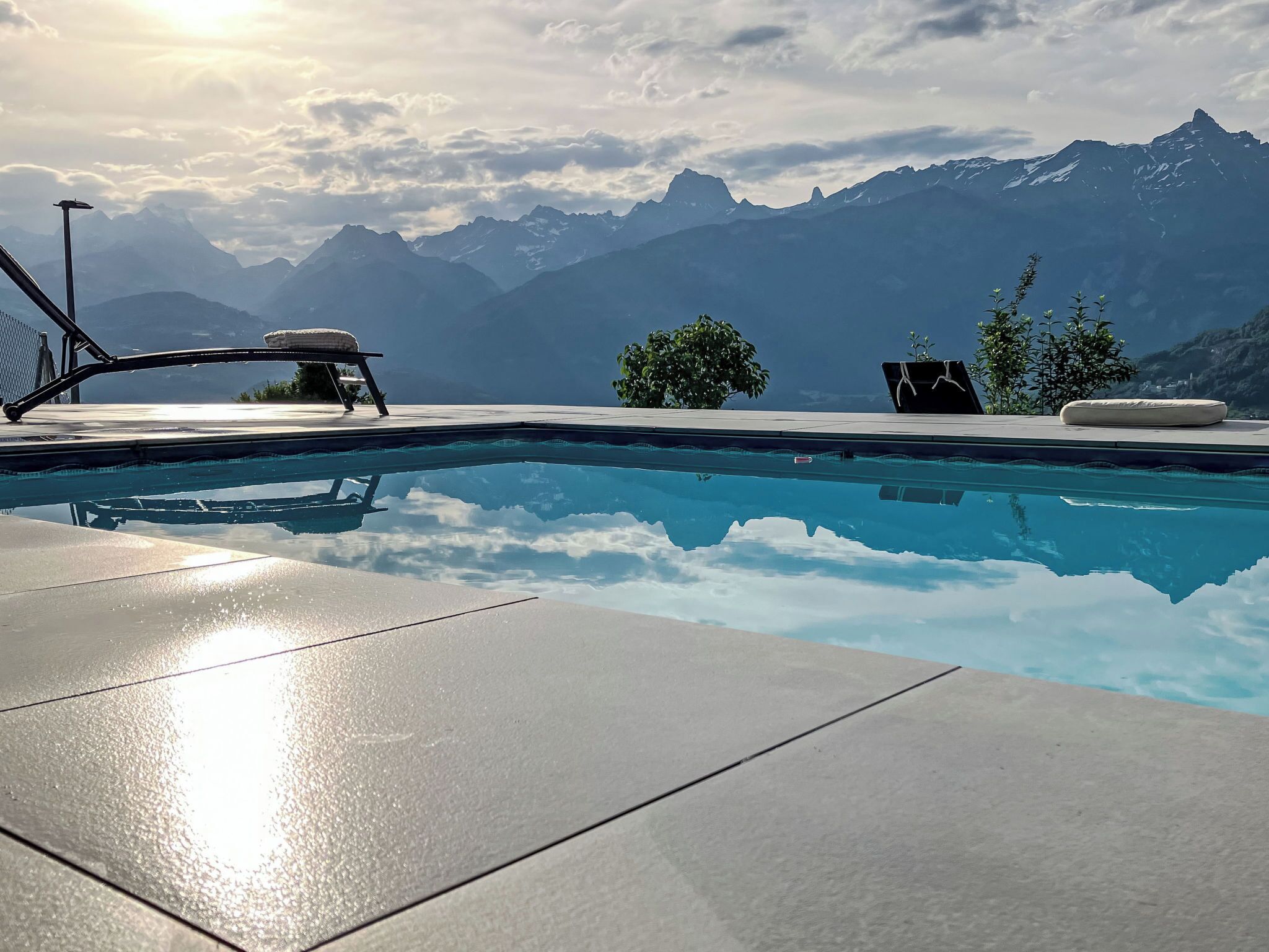 Une piscine avec vue sur les montagnes, des chaises longues et un petit arbre.