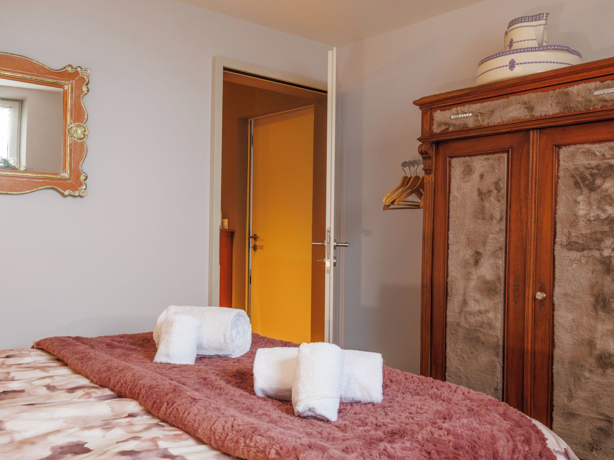 Ein Zimmer mit einem Bett, einem Schrank, einem Spiegel und einer Tür.