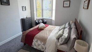 A bedroom with a bed, bedside table, lamp, dresser, window, and a hanging light fixture. - The Landmark Comfy 2BR Home in Rugby Sleeps 5 (Rugby)