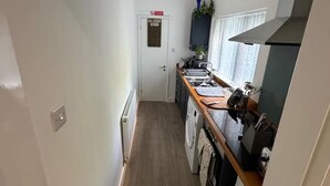 A narrow hallway leading to a kitchen with a washing machine, a stove, and a window with curtains. - The Landmark Comfy 2BR Home in Rugby Sleeps 5 (Rugby)