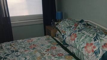 A room with a bed, a window with curtains, a bedside table with a lamp, and a wall with a floral pattern.